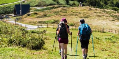 Two pilgrims with backpacks and walking poles on a green Camino de Santiago trail in Holy Year 2027
