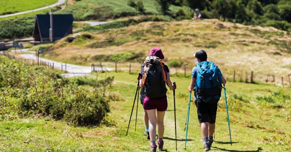 Two pilgrims with backpacks and walking poles on a green Camino de Santiago trail in Holy Year 2027
