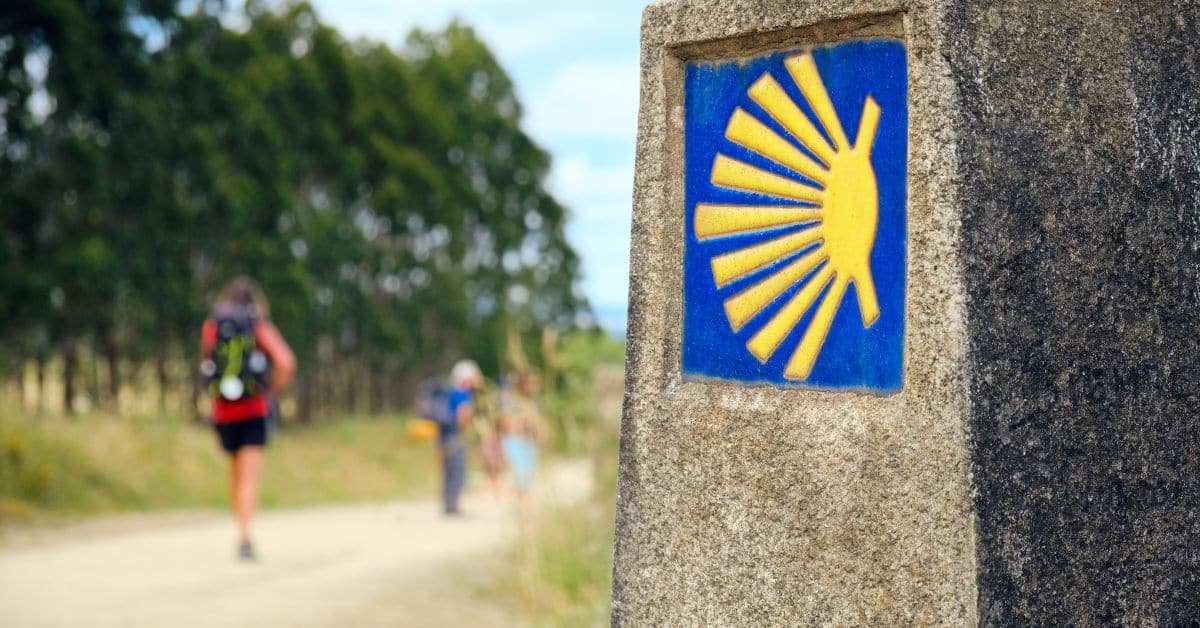 Pilgrims walking the Camino de Santiago in 2027 Holy Year, with scallop shell waymarker in the foreground