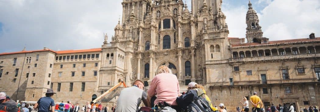 Two pilgrims seen from behind, looking up at Santiago de Compostela Cathedral at the end of their Camino