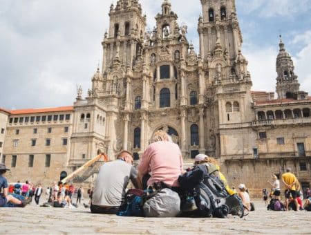 Two pilgrims seen from behind, looking up at Santiago de Compostela Cathedral at the end of their Camino