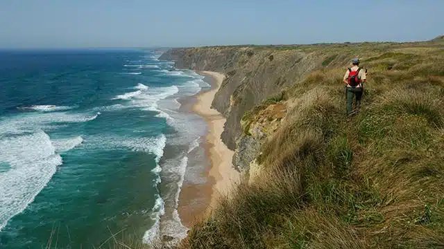 Walker on a clifftop path above a long Atlantic beach on the Rota Vicentina