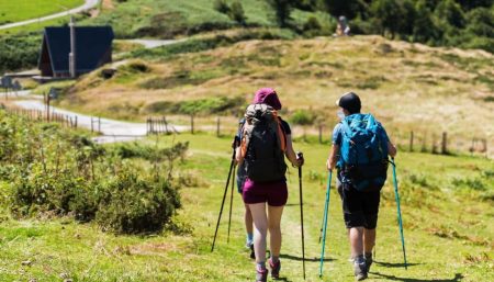 Two pilgrims with backpacks and walking poles on a green Camino de Santiago trail in Holy Year 2027