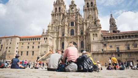 Two pilgrims seen from behind, looking up at Santiago de Compostela Cathedral at the end of their Camino